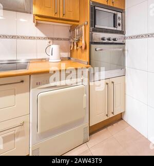 New stylish bright kitchen with wooden cabinets, microwave and oven. Spacious modern fully equipped appliance interior with wooden desk, ceramic stove Stock Photo