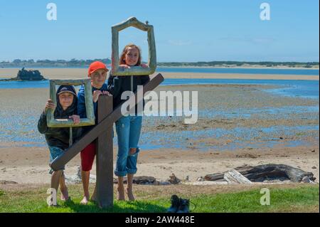 Siblings line up at Siletz Bay Park wooden picture frames for their picture with intertidal rocks in the background while on vacation in Lincoln City, Stock Photo