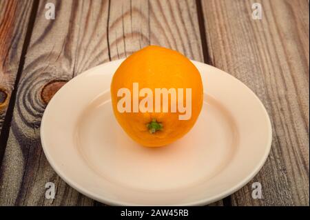 Ripe yellow lemon on a white plate on a wooden background. Close up Stock Photo