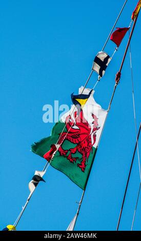 The red dragon flag of wales with tattered edge flying in the brisk breeze with pennants of many colours off tall ships rigging. Stock Photo