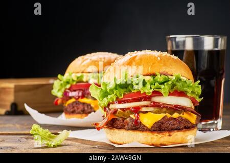 Delicious hamburgers and glass of drink on dark wooden table. Fast food concept Stock Photo