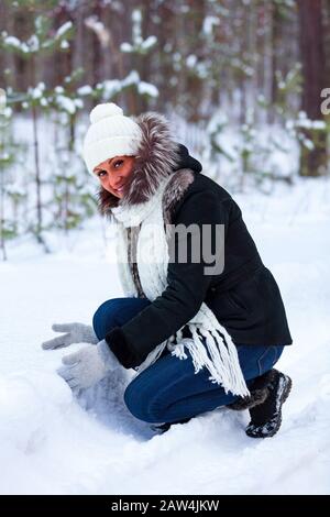 Woman playing with snow in a winter forest. Happy lady makes a snowball Stock Photo