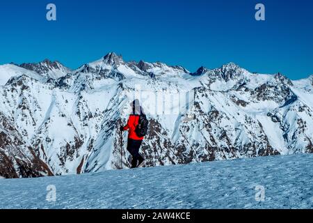 Tourist with backpack and trekking poles walking walking in the snowy mountains at sunny day. Stock Photo