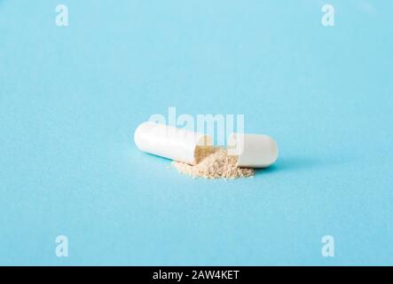 Side view of single white color gel capsule opened, yellow powder spilled out, on light blue background. Pharmaceutical concept. Lot of copy space. Stock Photo