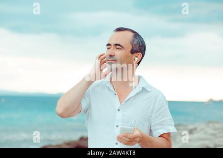 Who does not love music? Closeup portrait smiling eyes closed man listening to music enjoying nature by the sea hand on ear. Traveling happiness conce Stock Photo