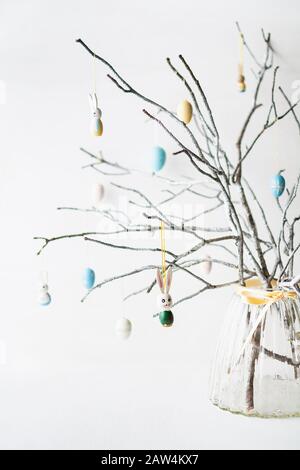 Still life with tree branches decorated with Easter eggs, feathers and bunnies in a glass vase. Vertical orientation Stock Photo