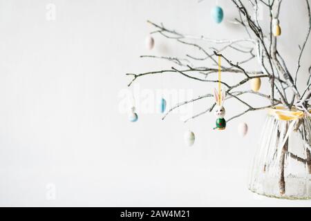 Still life with tree branches decorated with Easter eggs, feathers and bunnies in a glass vase Stock Photo