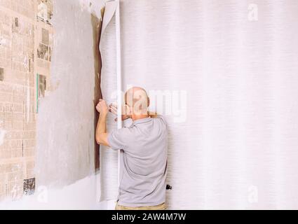 Man hanging a minimalist gray pattern paper wallpaper on wall. Lot of room for copy space. Stock Photo