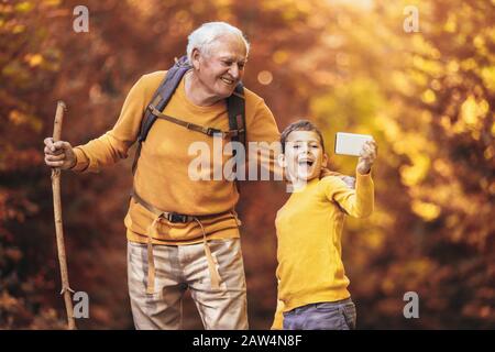 Grandfather and grandson hiking together in autumn park, make selfie photo. Stock Photo