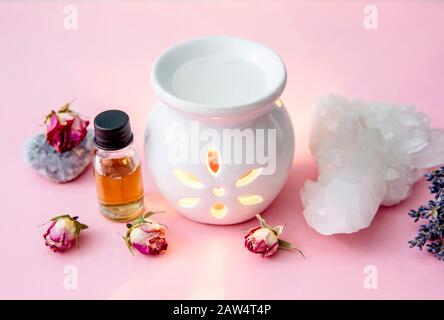 White ceramic candle aroma oil lamp with essential oil bottle and dried flowers, crystal geodes on modern pastel pink and blue background indoors. Stock Photo