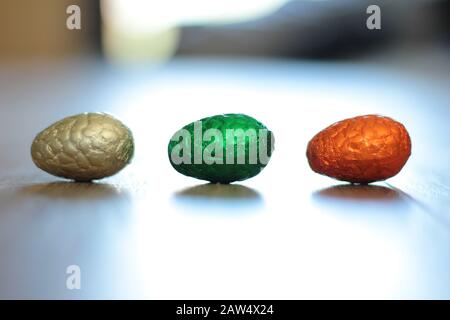 A portrait of three chocolat easter eggs in colorful tin foil lying on the floor in a row inside a house ready  to be found by children on their egg h Stock Photo