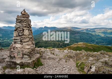 Summit cairn on the top of Loughrigg in the English Lake District with a view of the Langdale Pikes in the distance. Stock Photo