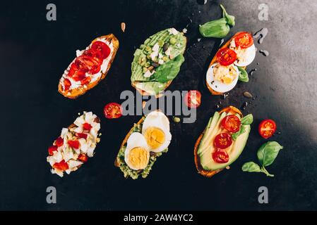 Sweet potato toasts with avocado, boiled eggs, tomatoes and sesame seeds on dark background. Healthy meal concept. Clean eating, Pescetarian food, top view Stock Photo