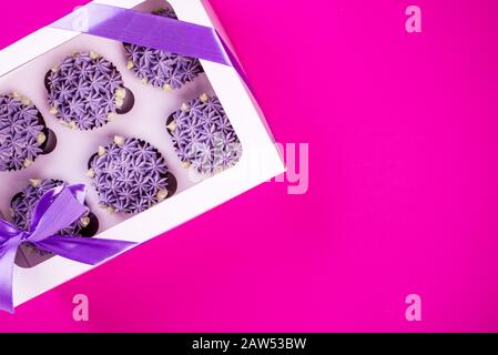 Delicious shawn cupcakes with curd cream in the form of flowers on a pink background. White cupcake packaging. Stock Photo