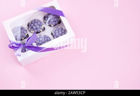 Delicious shawn cupcakes with curd cream in the form of flowers on a pink background. White cupcake packaging. Stock Photo