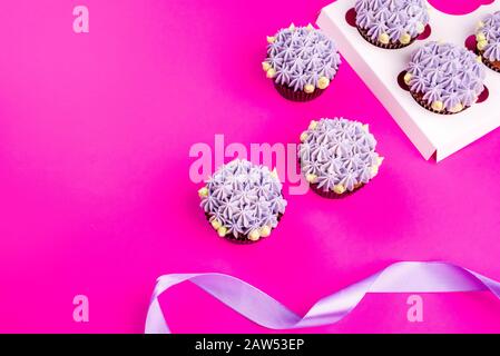 Delicious shawn cupcakes with curd cream in the form of flowers on a pink background. White cupcake packaging. Stock Photo