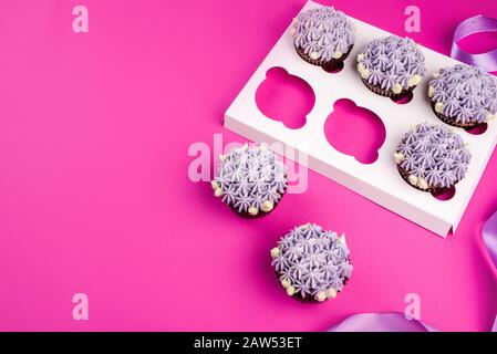 Delicious shawn cupcakes with curd cream in the form of flowers on a pink background. White cupcake packaging. Stock Photo