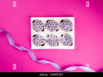 Delicious shawn cupcakes with curd cream in the form of flowers on a pink background. White cupcake packaging. Stock Photo