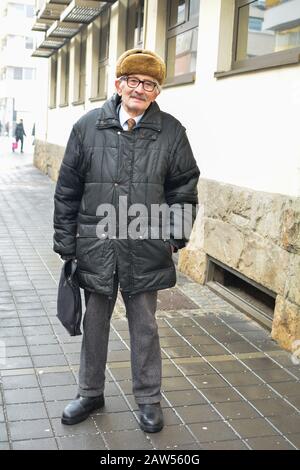 Active senior with fur cap, eyeglasses and briefcase walking in the street Stock Photo