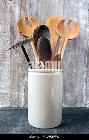 Eco friendly kitchen utensils including wooden spoons in vintage pottery container on wooden background Stock Photo