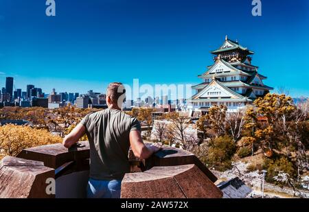 Young man is looking on  Osaka Castle from the view point. It is park with cherries. Stock Photo