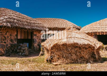 Traditional folk village. Thatched houses and blue sky. Straw hut roofs and clay walls with stones are still in a good condition. Stock Photo