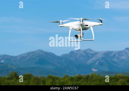 Quadcopter drone DJI Phantom 4 Pro flying, and takes pictures professional digital camera 4K over forest on background of mountains on sunny day Stock Photo