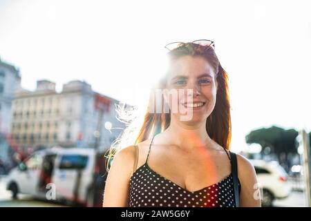 Optimistic young woman in trendy clothes cheerfully smiling and looking at camera while standing on city street on sunny day in summer Stock Photo