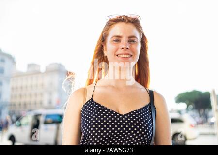 Low angle of happy young lady in stylish outfit friendly smiling for camera while standing on street and relaxing on weekend day Stock Photo