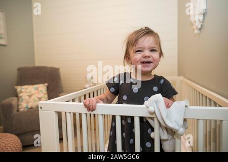 Portrait of cute toddler girl in her crib in bedroom. Stock Photo