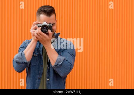Portrait of a young man taking a photograph over orange background Stock Photo