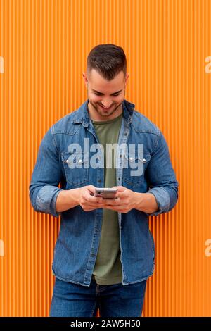 Portrait of a young cool man over orange background. The man is checks his cell phone. Stock Photo