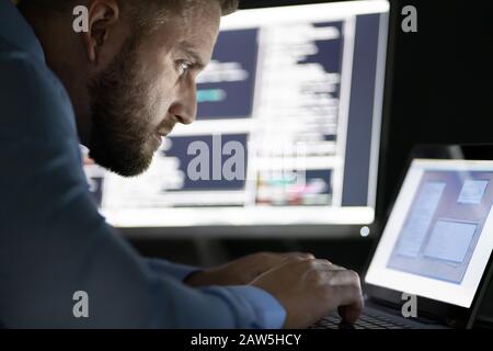 Programmer Working Late At Night On Multiple Computer Screens Stock Photo