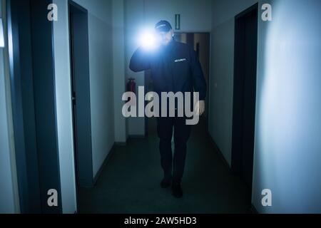 Security Guard With Flashlight Walking In Building Corridor Stock Photo