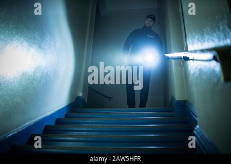 Male Security Guard Searching On Stairway With Flashlight Stock Photo