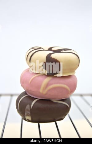 Close-up of three donuts of different flavors and colors stacked on a rack and with white background Stock Photo