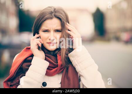 Phone talk. Portrait frustrated beautiful woman speaking on the mobile phone in a city street unfocused background having headache head pain problem s Stock Photo