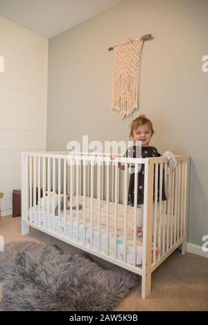 Portrait of cute toddler girl standing inside her crib Stock Photo