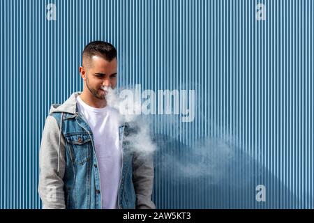 Young man smoking with an electronic cigarette over blue background Stock Photo