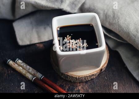 A still life shot with soy sauce in a vessel, two bamboo chopsticks and a cloth on a wooden surface Stock Photo