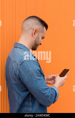 Portrait of a young cool man over orange background. The man is checks his cell phone. Stock Photo