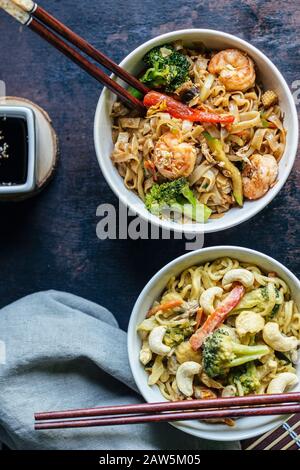 Overhead flat lay shot of two bowls full of thai noodles with vegetables, seafood, and cashews. Vertical image Stock Photo