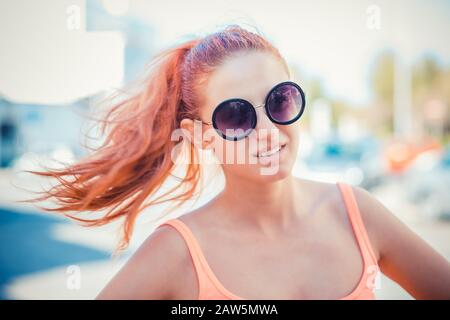 Smiling beautiful young woman in pink shirt and round sunglasses enjoying time outdoors in summer holiday time. beauty outdoor portrait with city stre Stock Photo