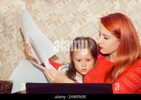 Mother with her child calculating home expenses. Busy Mother With child Running Business From Home looking at bank statement contract papers while kid Stock Photo