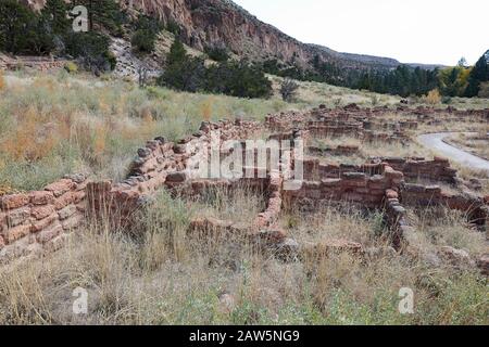 Part of the Tyuonyi ruins of the ancestral Pueblo peoples and unidentifiable hikers by the cliffs along the main loop trail in Frijoles Canyon at Band Stock Photo