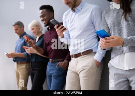 Row Of Diverse Businesspeople Using Phones In Office Stock Photo