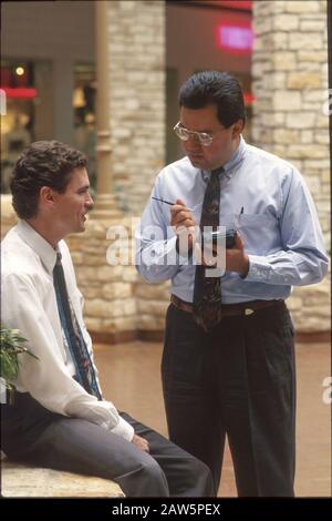 Austin Texas USA, 1990: Hispanic man uses Newton computer at shopping mall to collect market survey answers from Anglo man.  Model Release. ©Bob Daemmrich Stock Photo