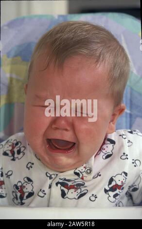 Five-month-old baby boy cries in high chair at home. Stock Photo