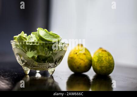 Raw cut aloevera or aloe vera gel in a glass bowl and some fresh ripe lemons or limbu or nimbo on wooden surface along with their reflection on the su Stock Photo