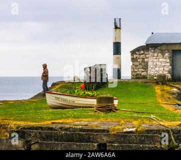 Carnlough-Northern Ireland, UK/May 19-2020:  Small harbor and lighthouse in fishing village under cloudy skies with a view of sea beyond. Stock Photo